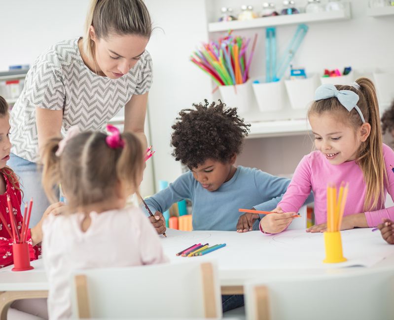 A teacher drawing with children at a preschool table